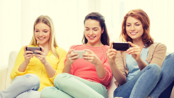 smiling teenage girls with smartphones at home